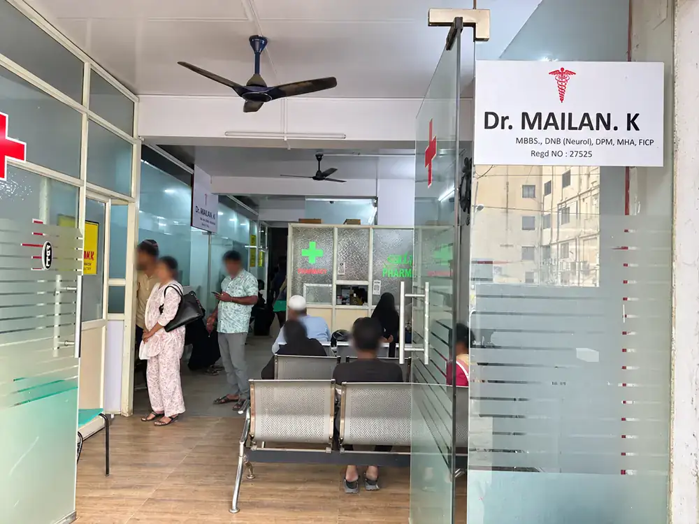 Inside the entrance: Dr. Mailan K's nameboard, the waiting benches and the pharmacy counter at the back. Faces are blurred